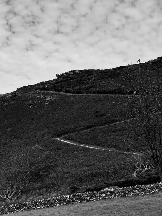Schwarzweißfoto: Hügel mit Pfad unter bewölktem Himmel